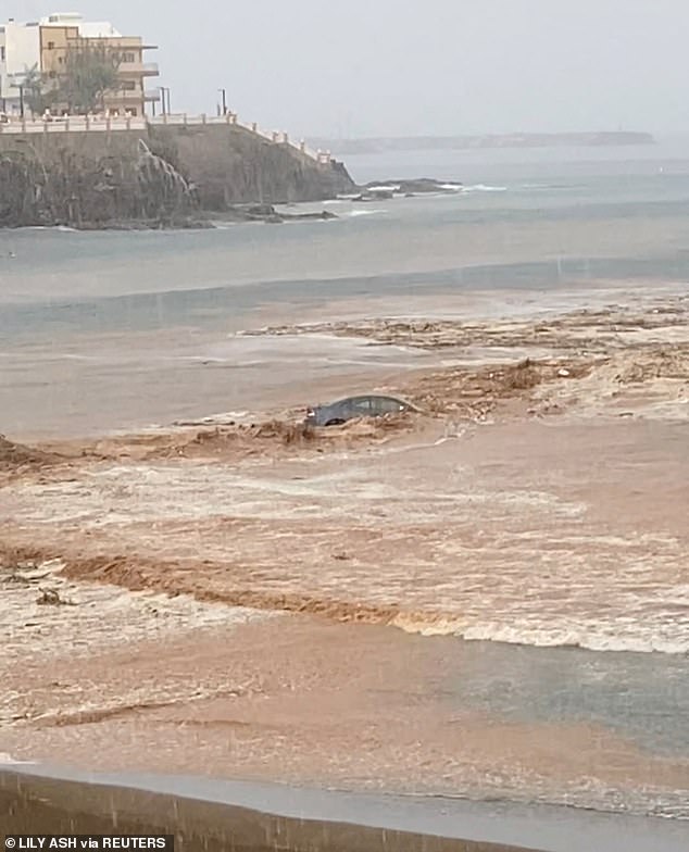 El automóvil fue empujado al mar por agua de color de suelo rápido en movimiento rápido