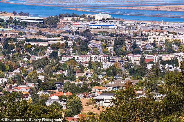 Vista aérea de San Carlos en Silicon Valley; áreas residenciales con casas construidas sobre colinas en primer plano; áreas industriales y la costa de la bahía de San Francisco en el fondo