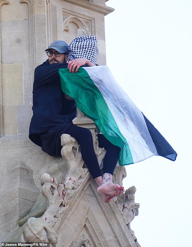 El manifestante se agarra sobre una bandera palestina mientras la sangre se vierte de sus pies sobre partes de la torre